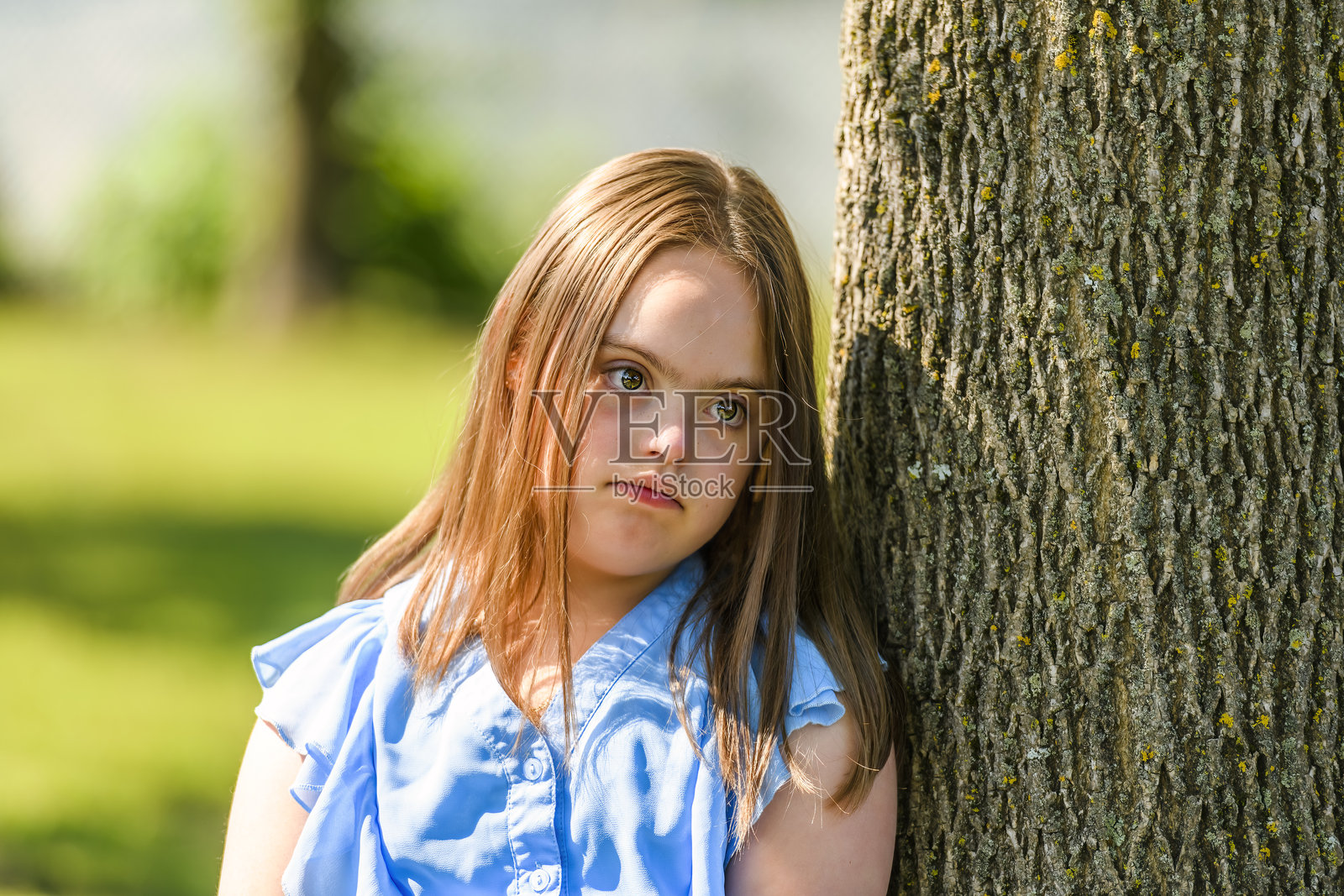 患有唐氏综合征的女孩在公园里，在树旁玩耍的肖像照片摄影图片
