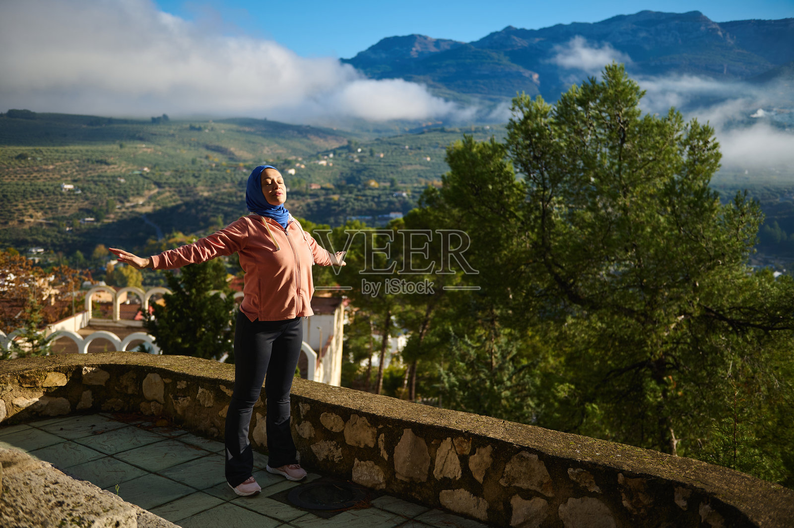 一位戴着头巾的放松的穆斯林阿拉伯女性站在风景优美的露台上，俯瞰群山照片摄影图片