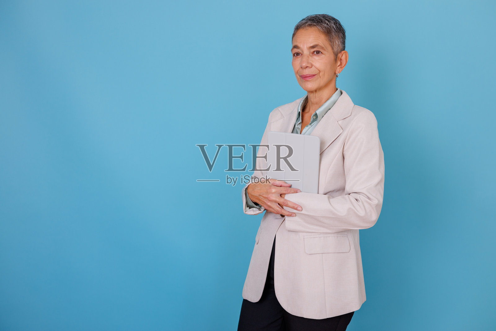 一位自信的成熟的女商人，手持数字平板电脑，背靠蓝色背景，若有所思地看向别处。照片摄影图片