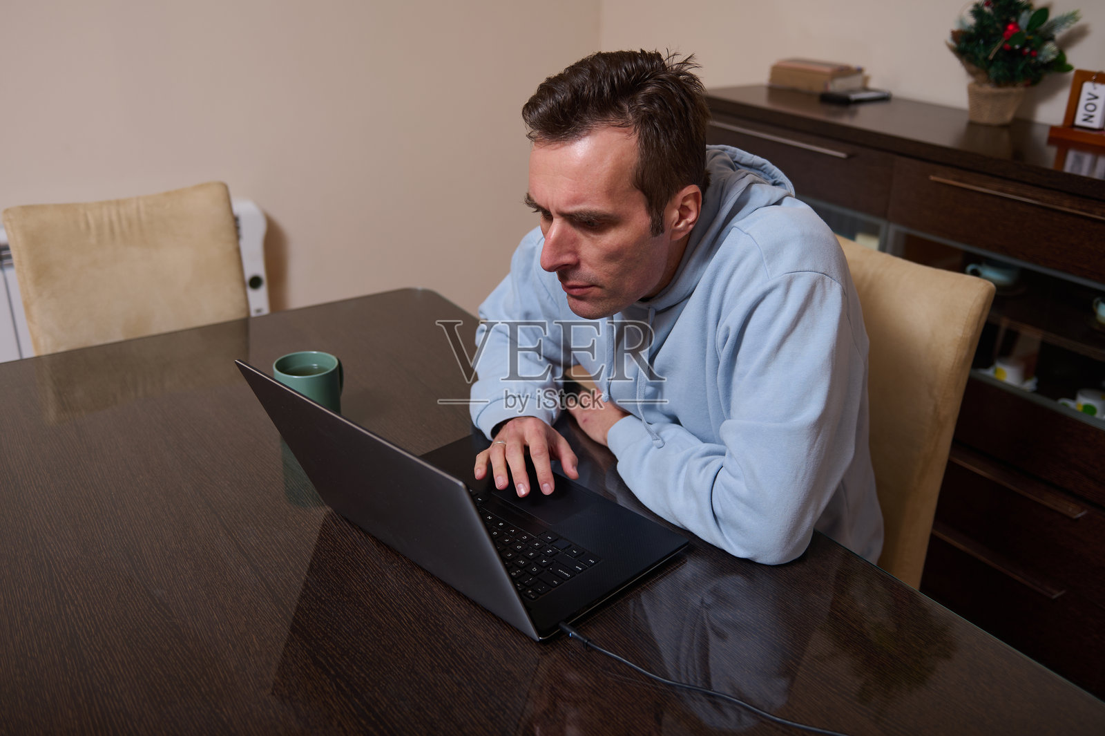 忙碌的居家办公日：年轻男子穿着连帽衫在餐桌上用笔记本电脑工作照片摄影图片