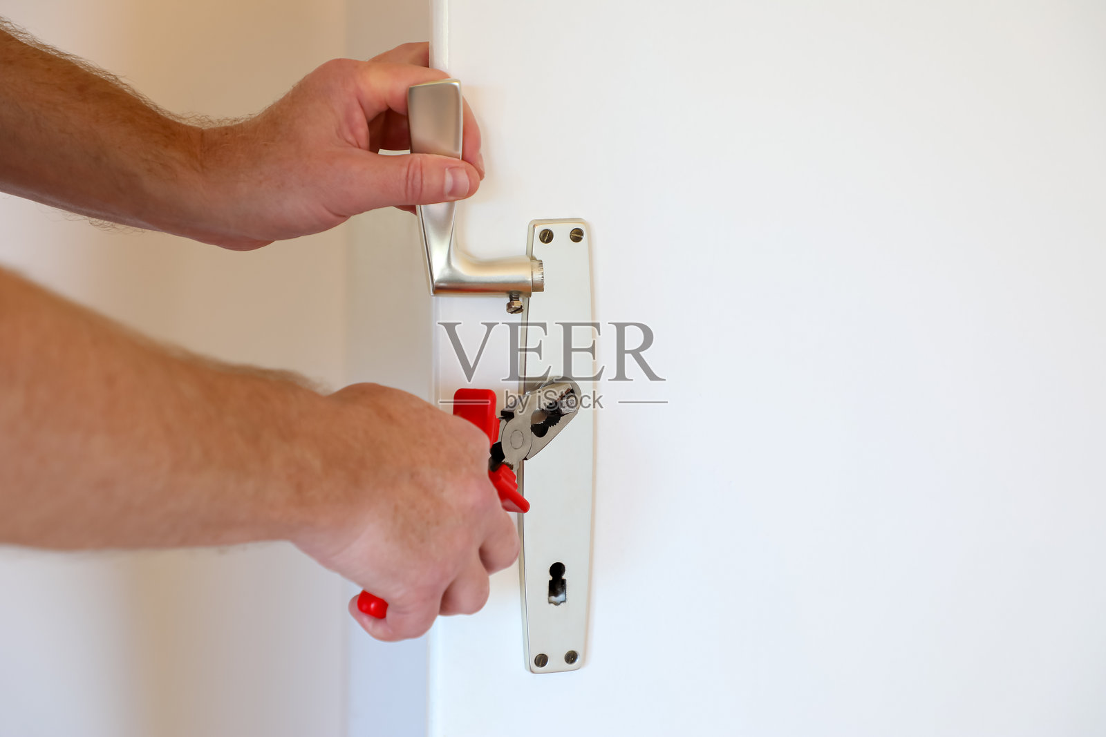 特写镜头展示男性双手使用钳子修理门把手和锁芯，展现居家维修和DIY工作。照片摄影图片