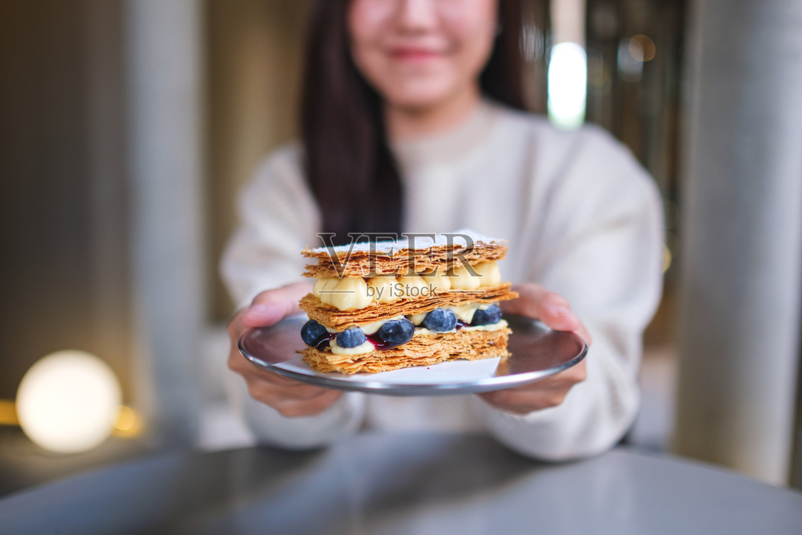 咖啡馆里，一位女士特写镜头，她正拿着并递上一块蓝莓千层酥照片摄影图片