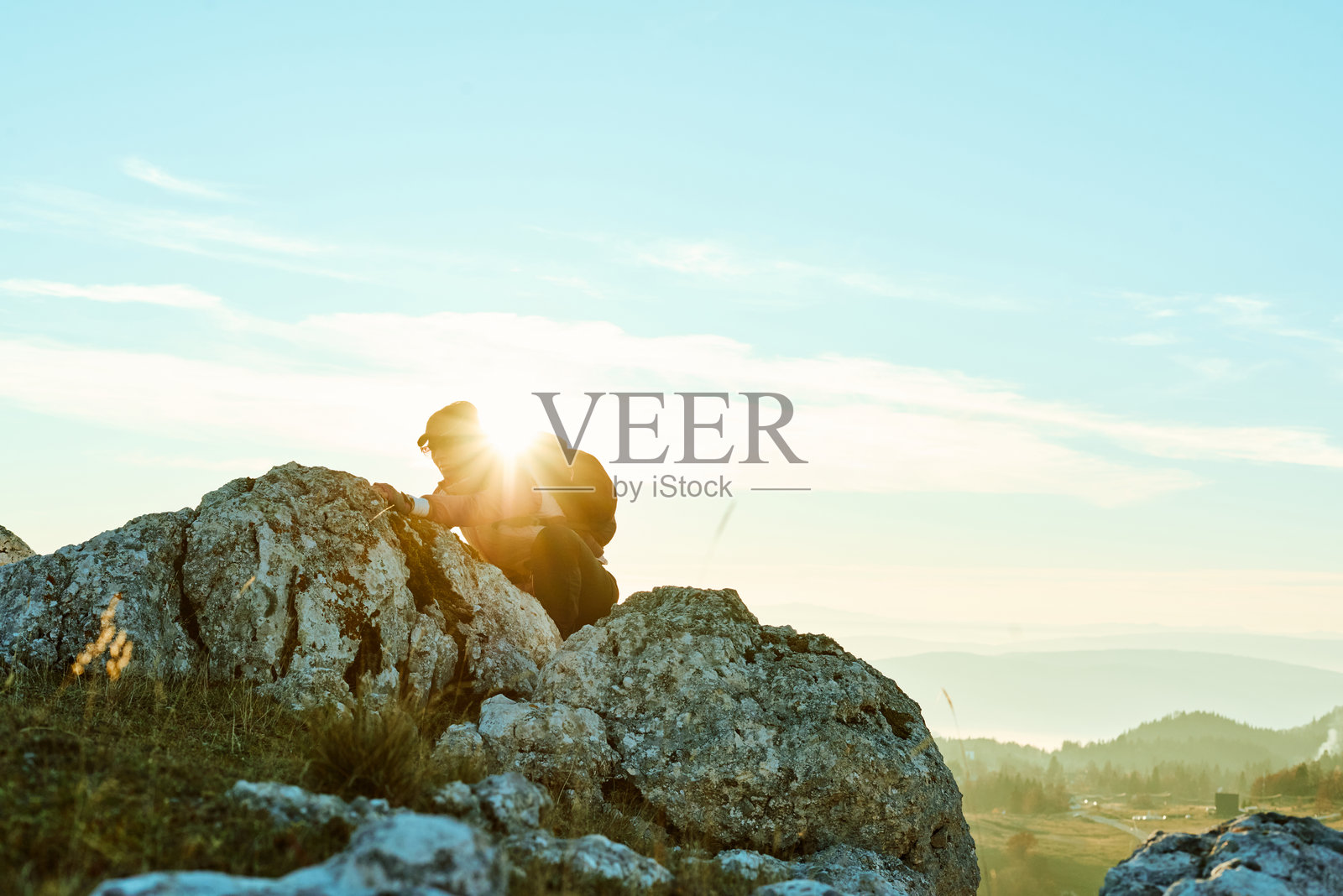 夕阳下，徒步者在晴朗天空下的山地景观中攀登崎岖的地形照片摄影图片