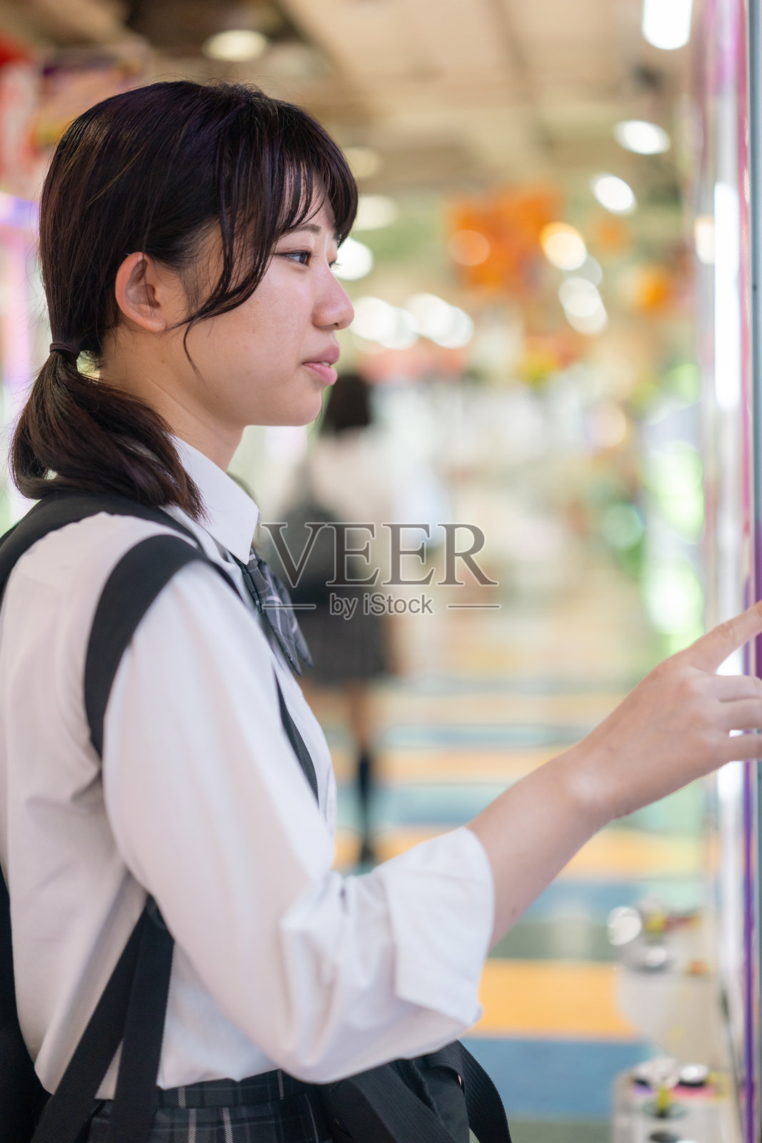 一名女高中生在游乐街机厅玩抓娃娃机照片摄影图片