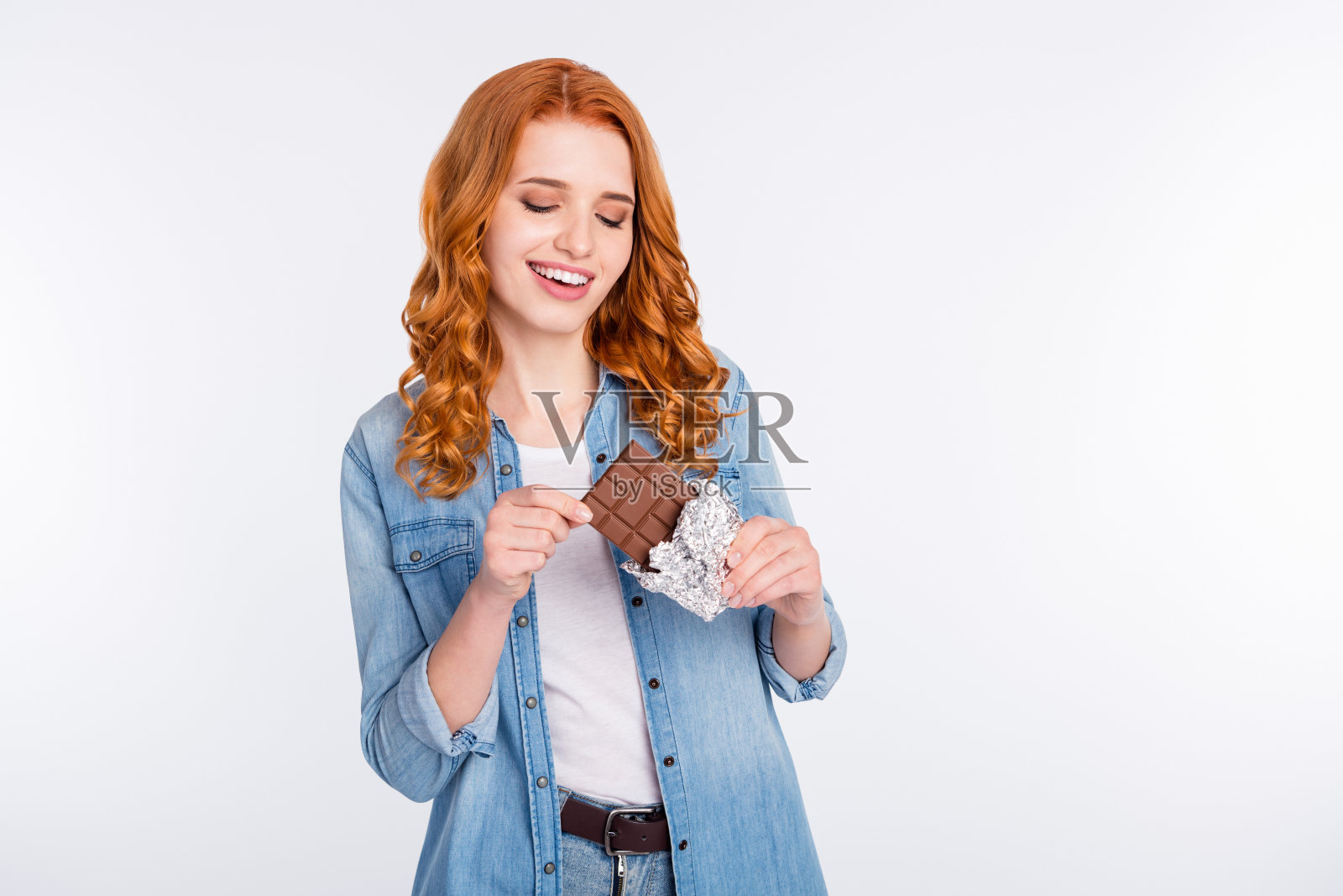 一位迷人的年轻女子，脸上洋溢着积极的神情，手中拿着巧克力，看起来很饿，背景为灰色。照片摄影图片