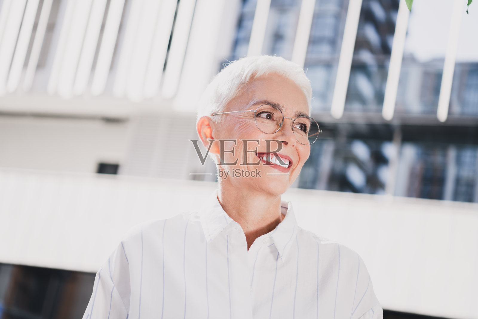一位优雅的年长女商人在现代城市建筑和日光下，带着职业氛围的商务风格，在城市户外环境中微笑照片摄影图片