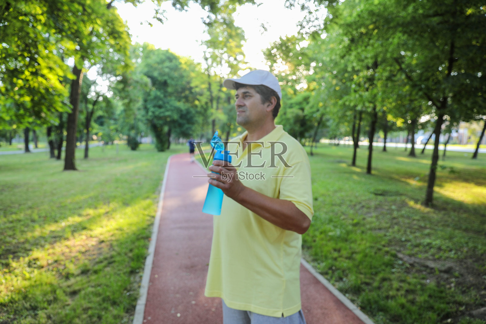 阳光明媚的日子里，一位老人正在公园里喝水照片摄影图片