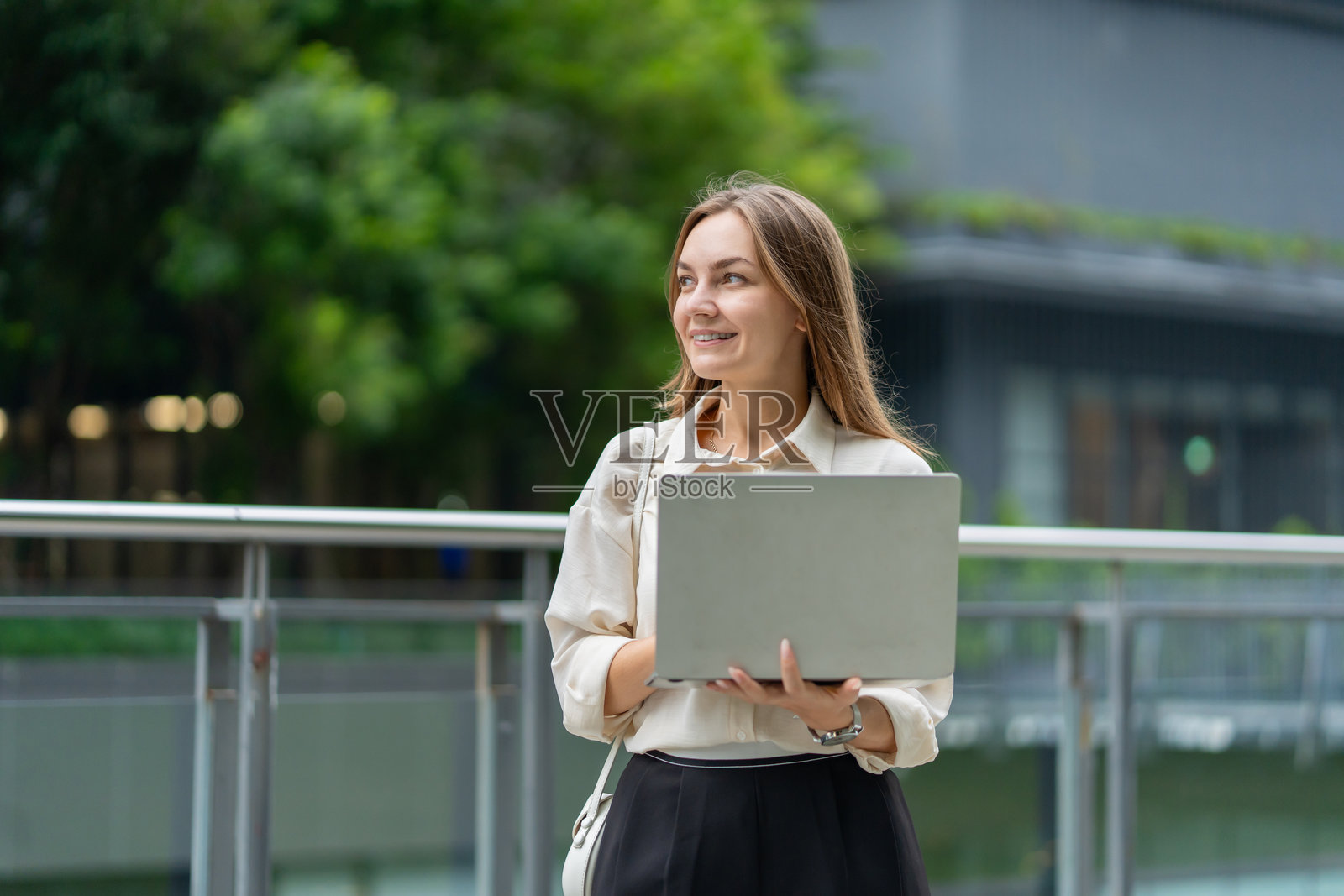 一位年轻的高加索女商人正在办公室外使用笔记本电脑。一位有魅力的年轻职业女性员工感到快乐和自信，享受都市生活、独立和事业成功。照片摄影图片