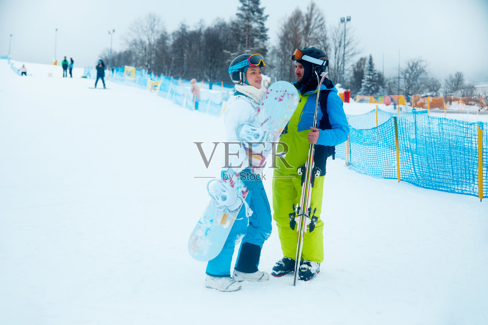 一对情侣在滑雪胜地享受冬日时光，雪板和滑雪板一应俱全，在阴天的午后于雪坡上谈笑风生。照片摄影图片