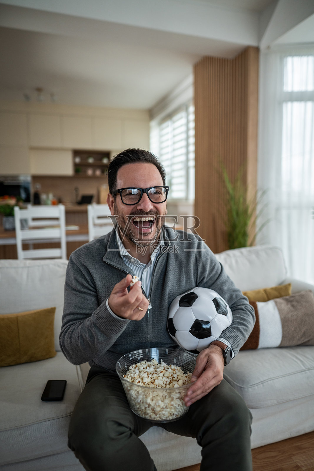 中年男子在家看足球，吃着爆米花，哈哈大笑照片摄影图片