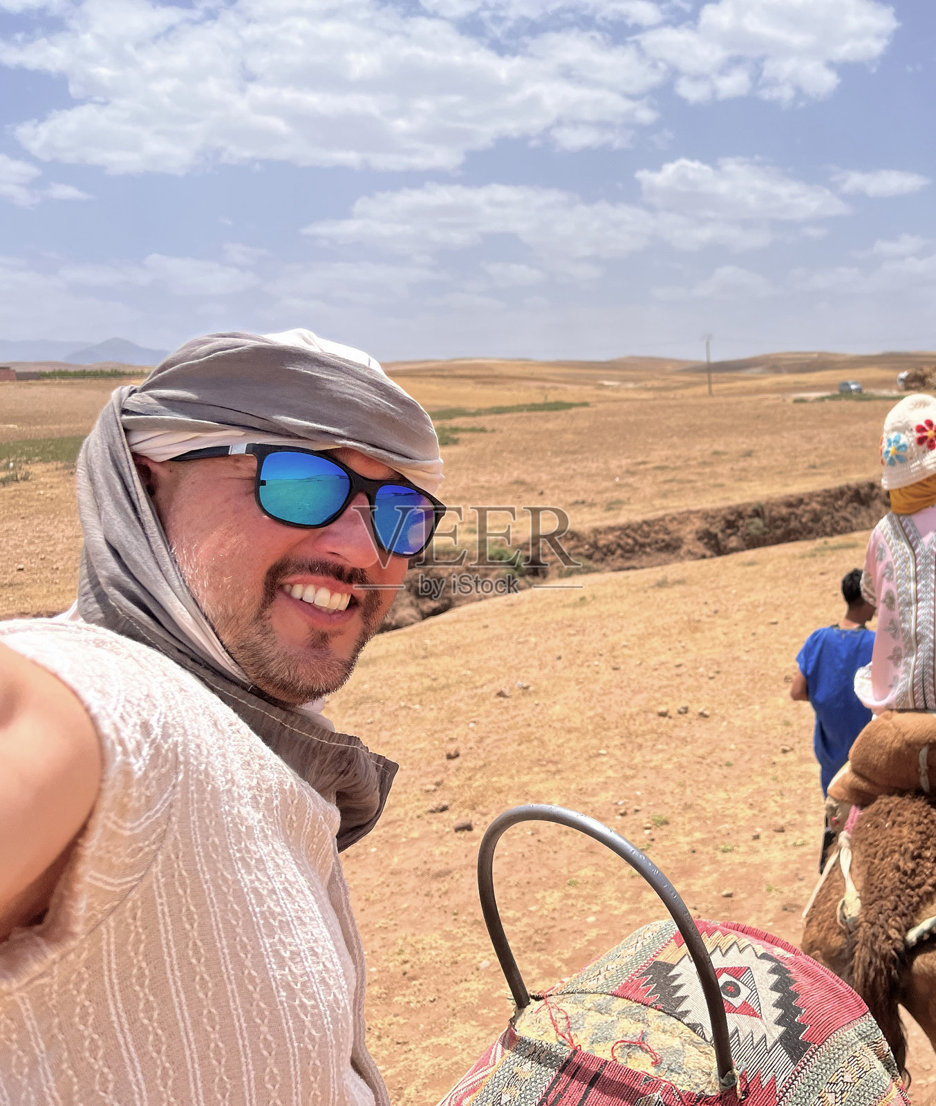 一名中年拉丁裔男性游客戴着头巾，在摩洛哥马拉喀什附近的撒哈拉沙漠中，与朋友们一起度假时自拍。照片摄影图片