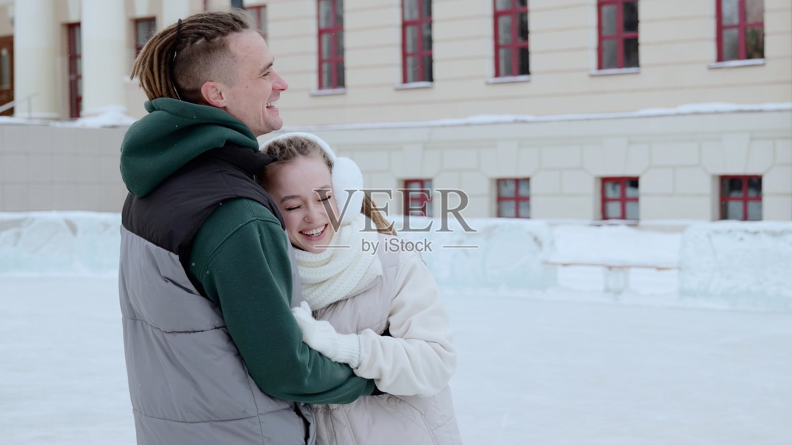 年轻情侣在溜冰场上笑着拥抱，周围环绕着迷人的冬季城市景观。一同享受着充满欢乐、温暖和节日气氛的浪漫一天照片摄影图片