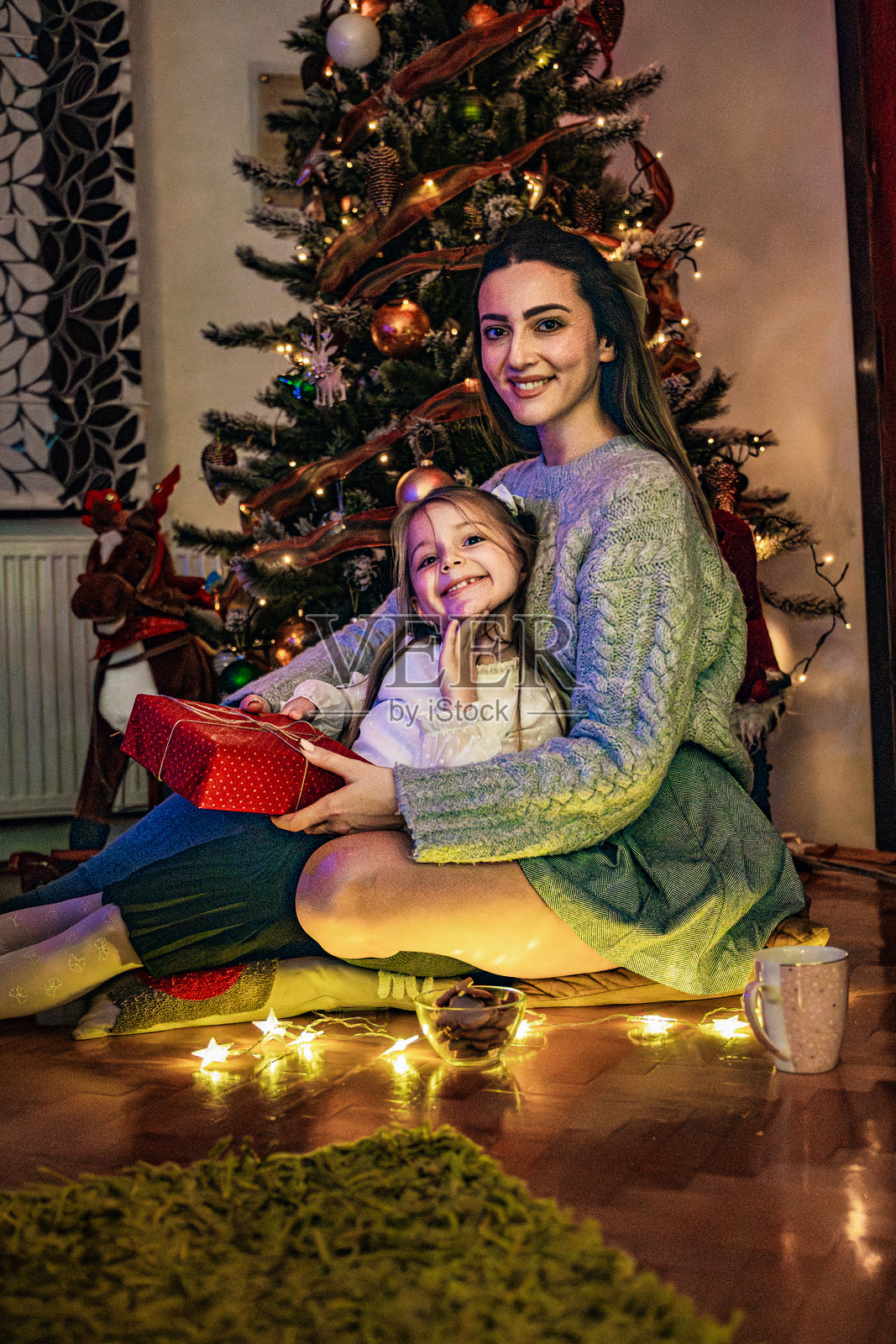 圣诞晚会上，母亲在圣诞树前给漂亮的女儿送礼物。包括节礼日、假日季和新年庆祝活动。照片摄影图片