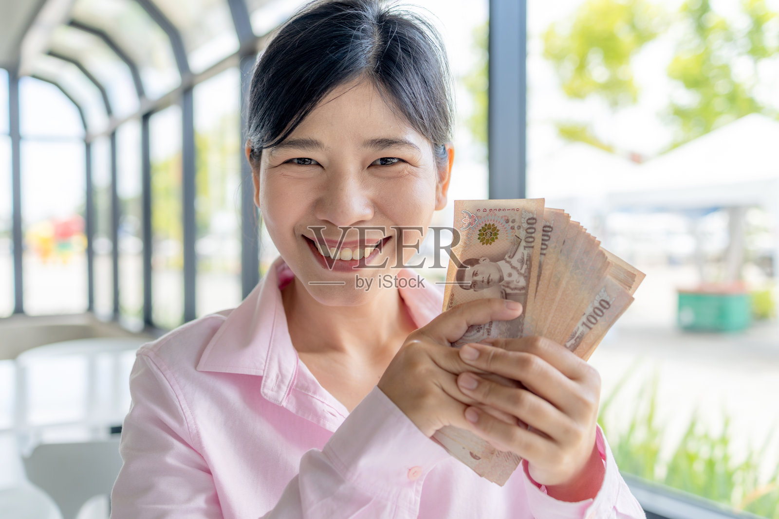 自信的亚洲女性手持泰铢纸币，象征着财富、现金、经济稳定、收入增长和个人成功。照片摄影图片