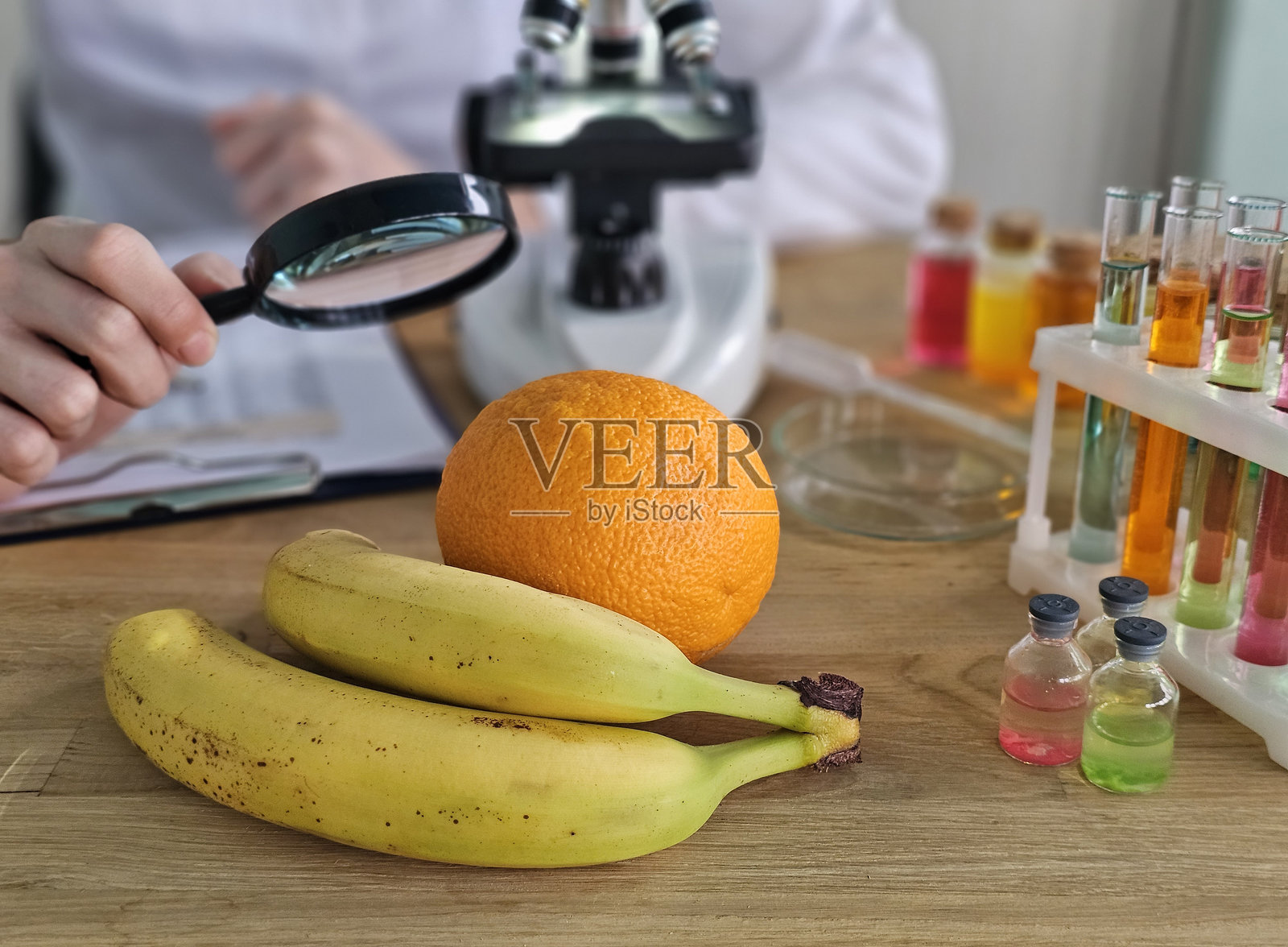 科学家在实验室里用放大镜检查水果，旁边有色彩斑斓的液体和显微镜照片摄影图片