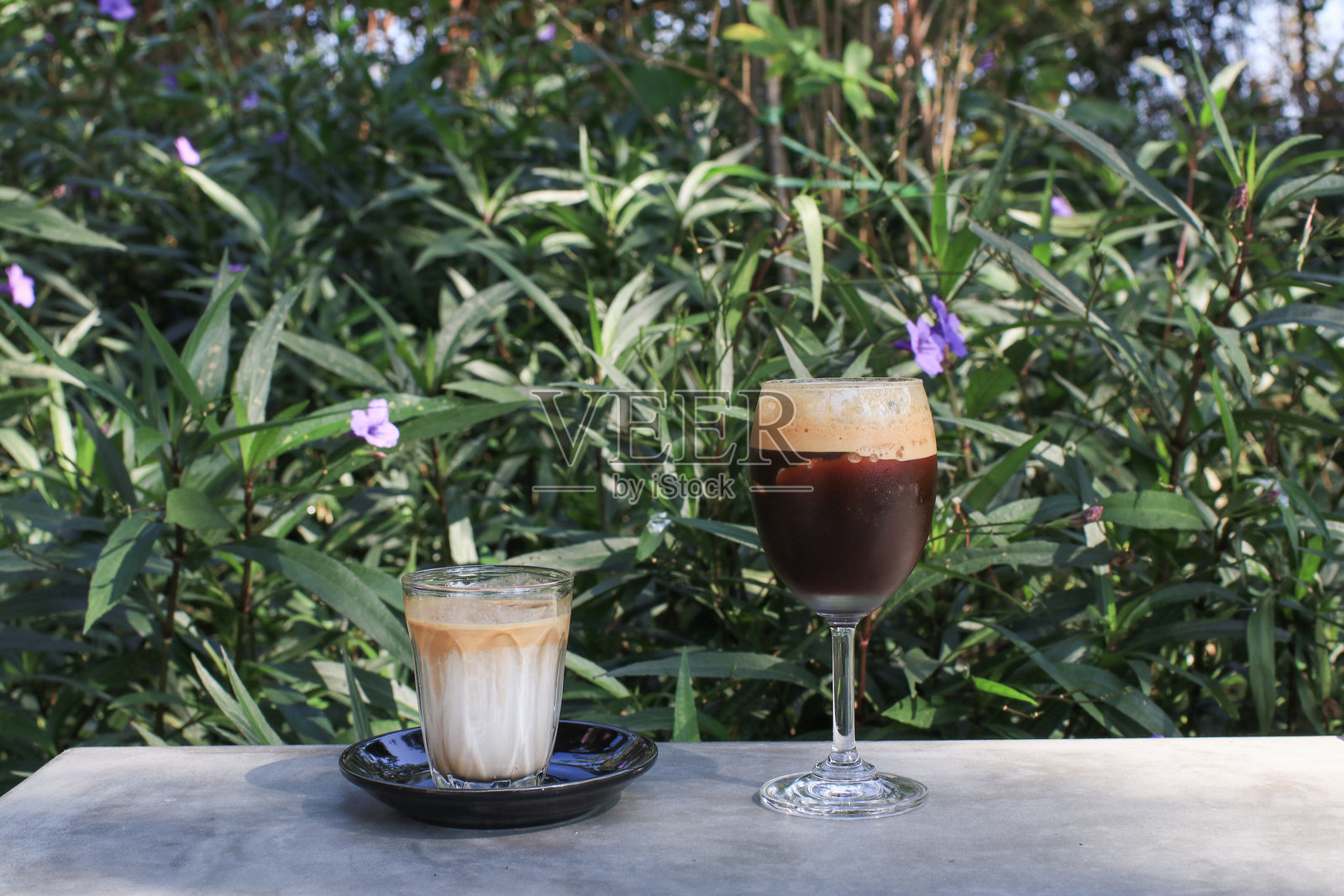 花园里脏咖啡和冰咖啡在灰色水泥地上摇晃。清爽的饮品与大自然。照片摄影图片