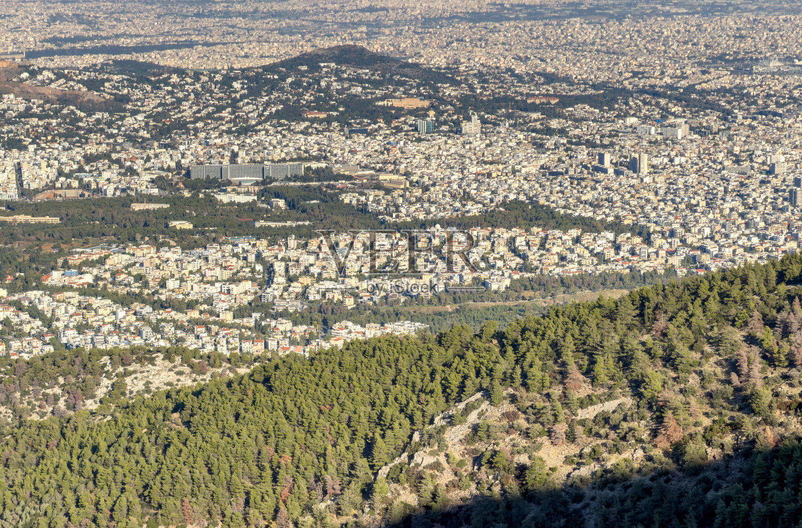 明媚午后，从海米托斯山俯瞰雅典城市景观，阳光照耀的林木山坡后是茂密的城市蔓延照片摄影图片