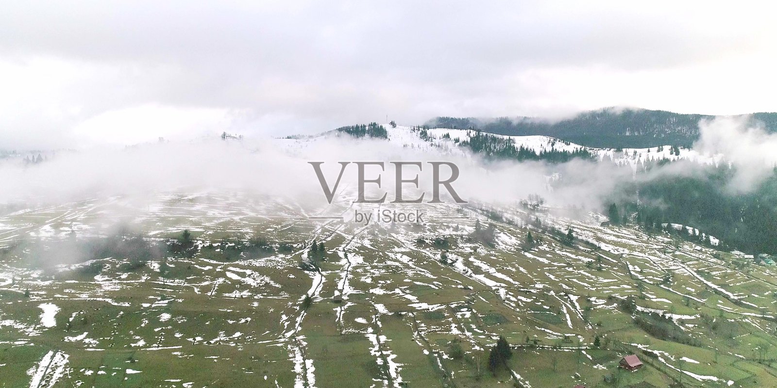 早晨的薄雾笼罩着绿色的田野，田野上散落着雪花。照片摄影图片