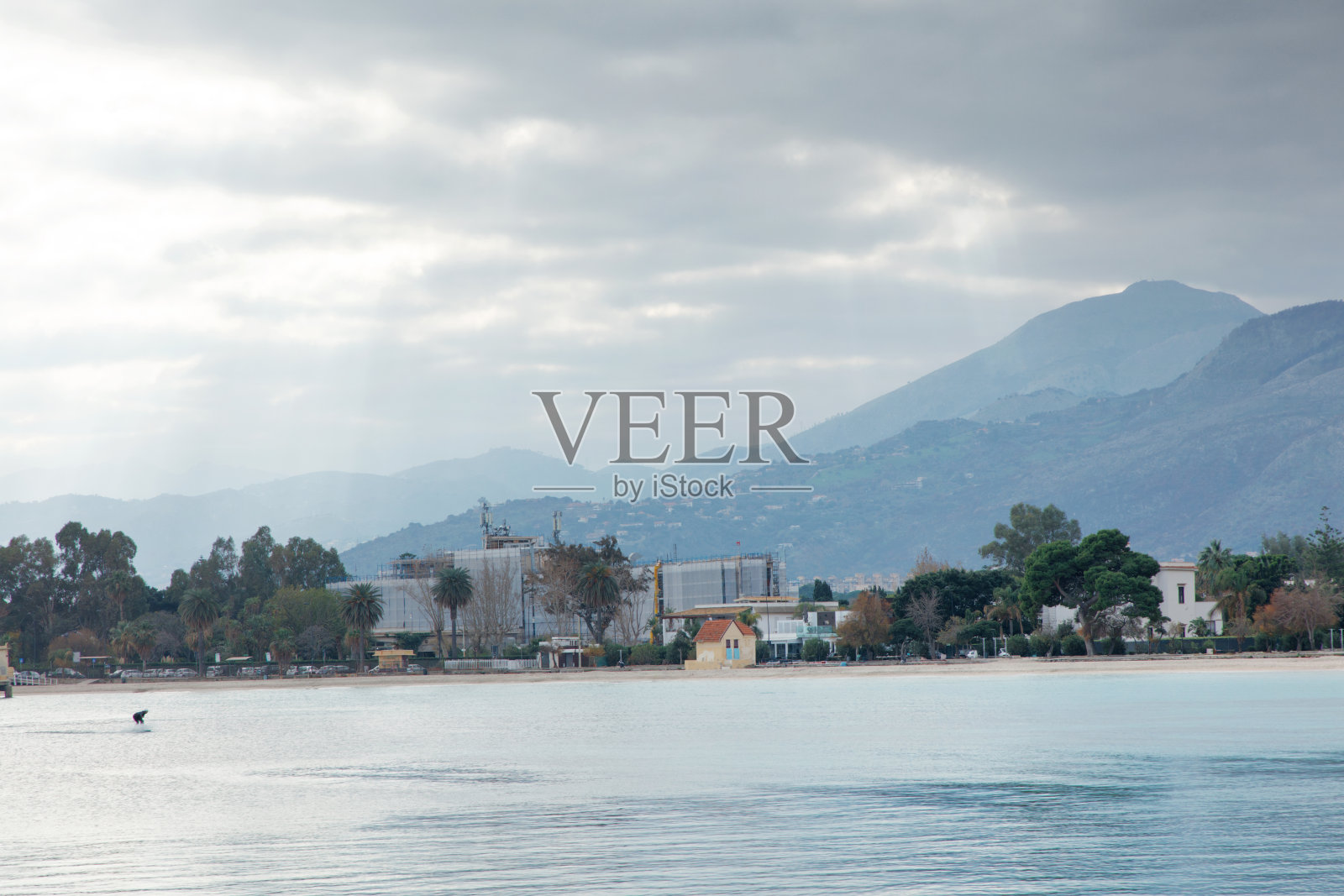 平静水域、棕榈树和山脉背景下的海滨小镇海滩景象照片摄影图片