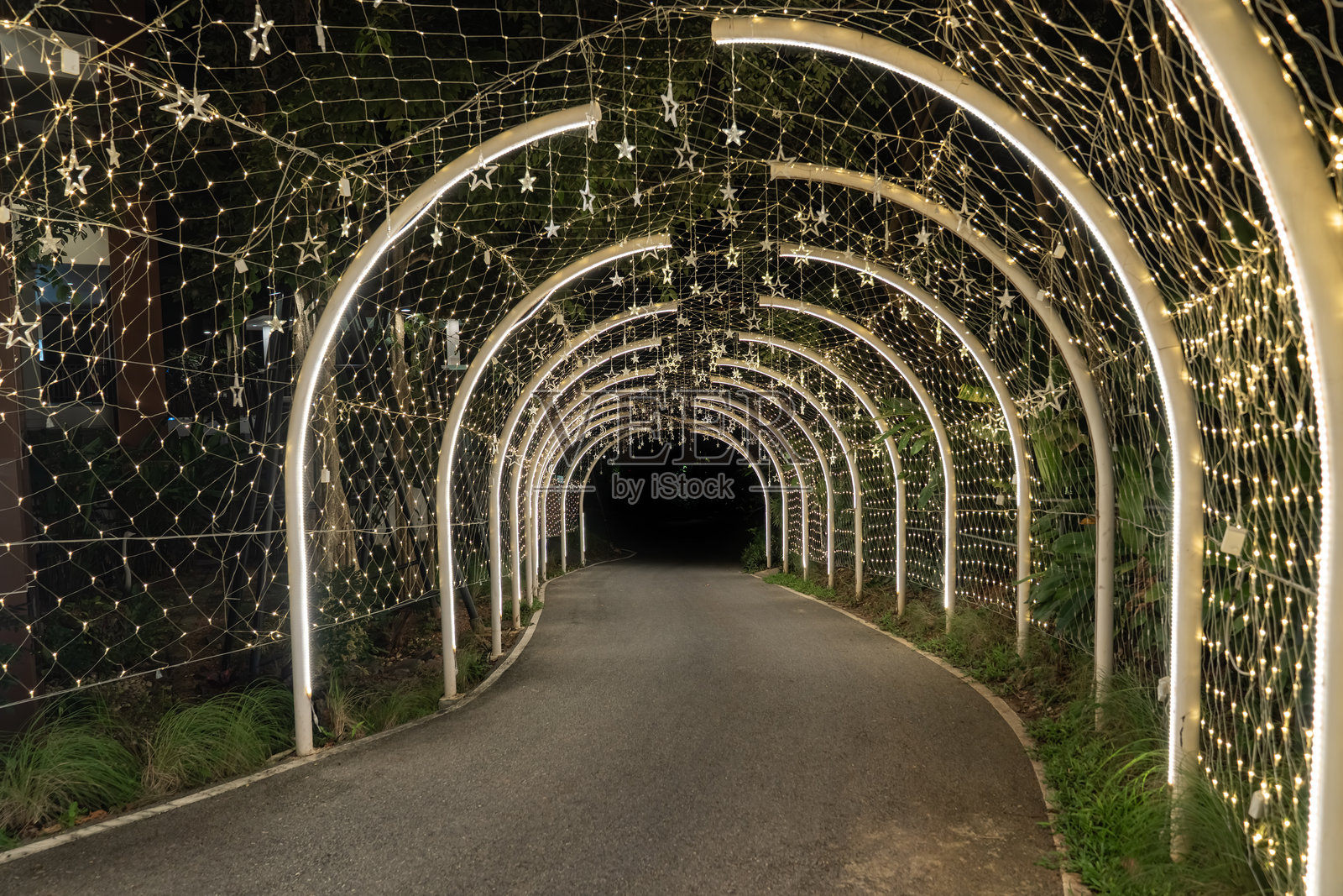 黑暗中，一条装饰着暖色灯光的弯曲隧道发出柔和的光芒，被照亮的拱门在宁静的夜景中引向小径。照片摄影图片