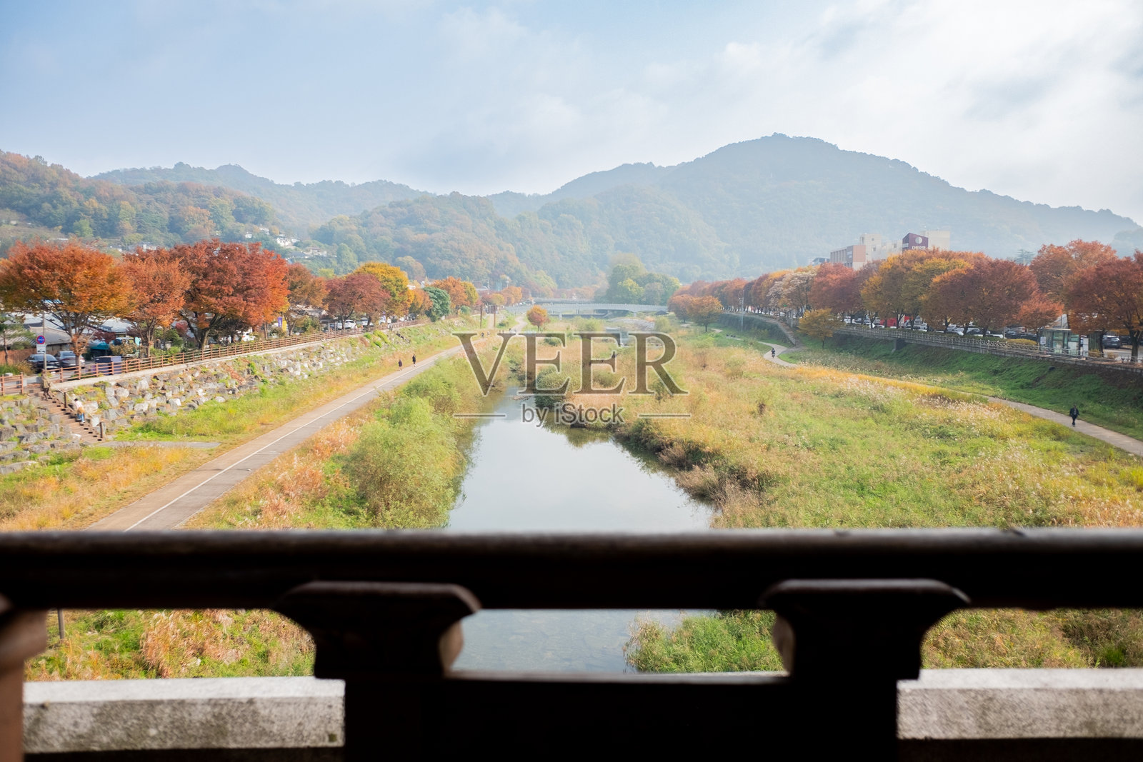 秋日河流在两岸的树林间流淌，树叶色彩斑斓，有步行道，背景是山峦。照片摄影图片