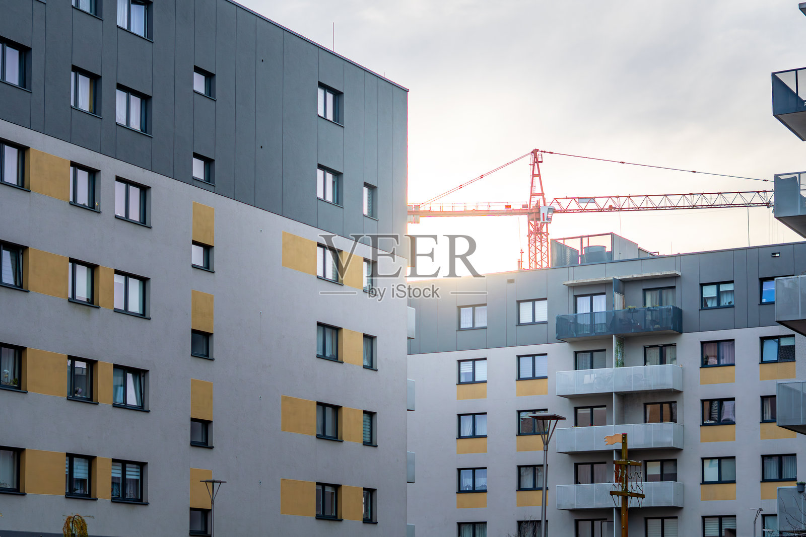 灰色与黄色外墙板的住宅楼，在明亮的蓝天背景下，前面可见一栋建筑起重机照片摄影图片