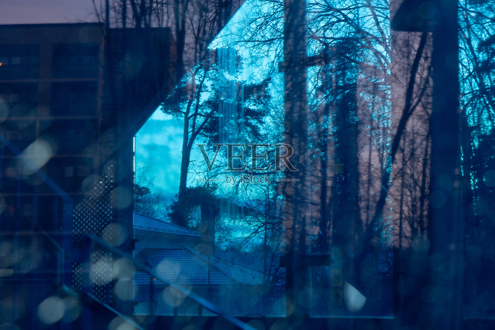 破碎的蓝色玻璃倒映着周围的环境——森林树木和房屋屋顶，营造出一种破碎、抽象且略带诡异的自然与都市元素景象照片摄影图片