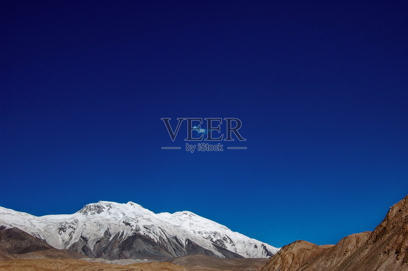 晴朗蓝天下，一座白雪皑皑的山峰，伴有一朵小小的云彩。照片摄影图片