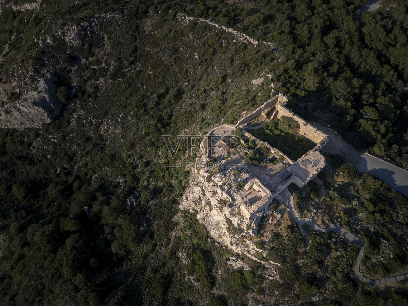 宏伟的城堡遗址坐落于崎岖的悬崖顶端，提供了一处历史地标景观，可以看到城堡及希腊罗德岛上葱郁的森林照片摄影图片