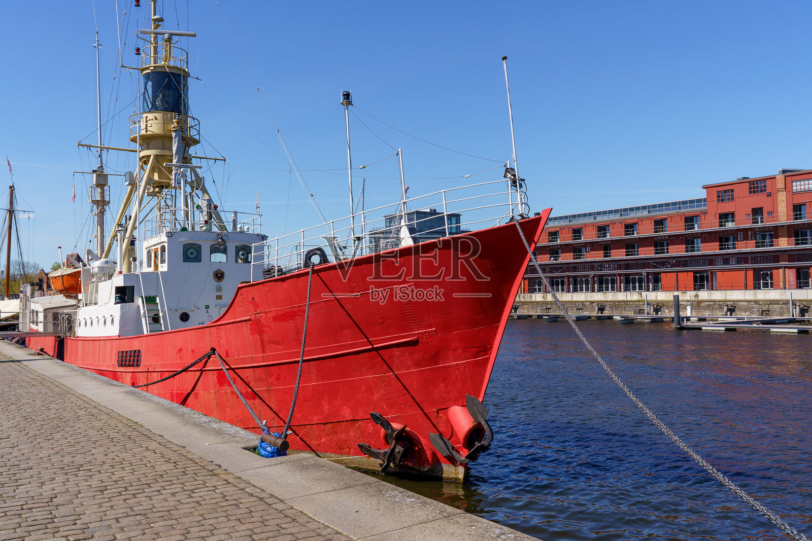 一艘大型红色船只停泊在德国吕贝克的码头。船只被链条和浮标环绕，海面和天空构成宁静祥和的背景。照片摄影图片