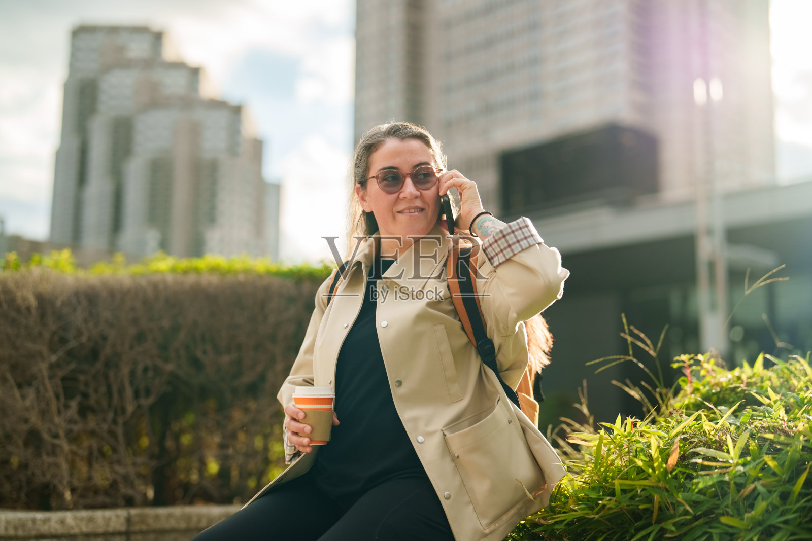 女性在城市景观背景下，一边喝咖啡一边打电话照片摄影图片