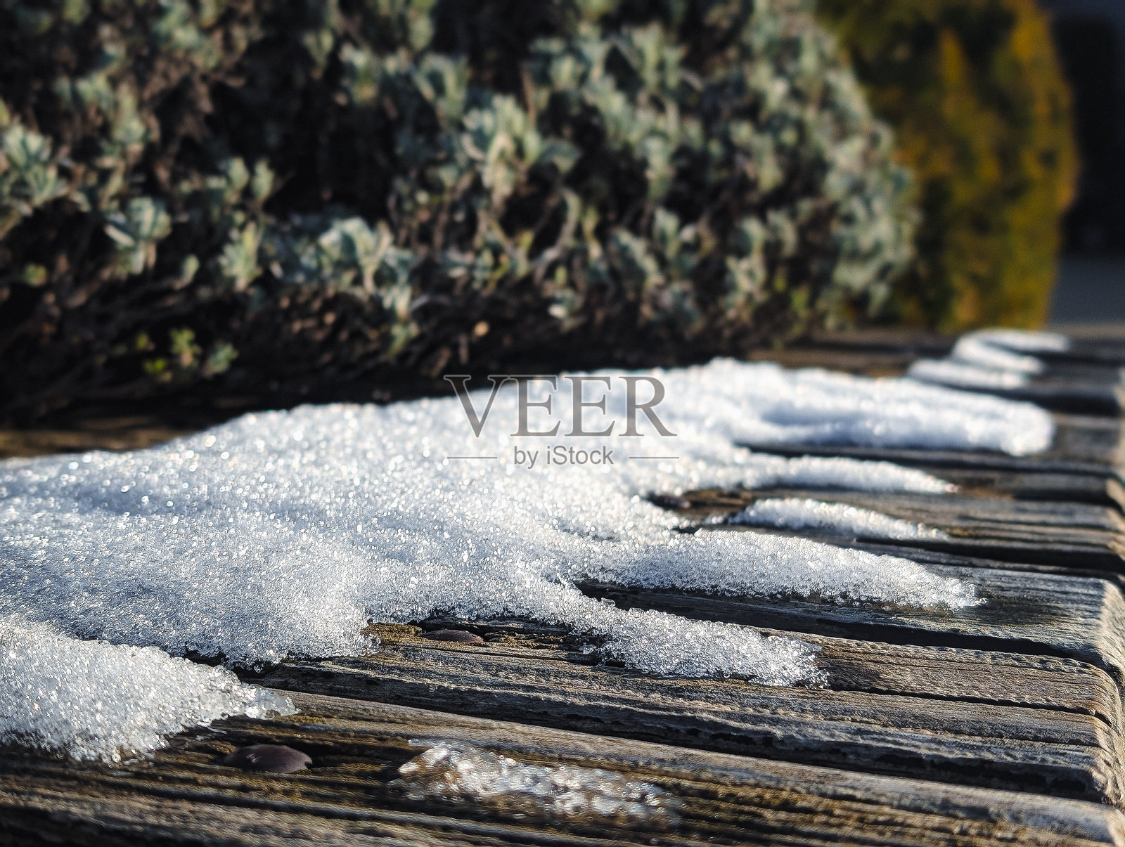 温暖的阳光下，木凳上融化的雪和冰晶照片摄影图片