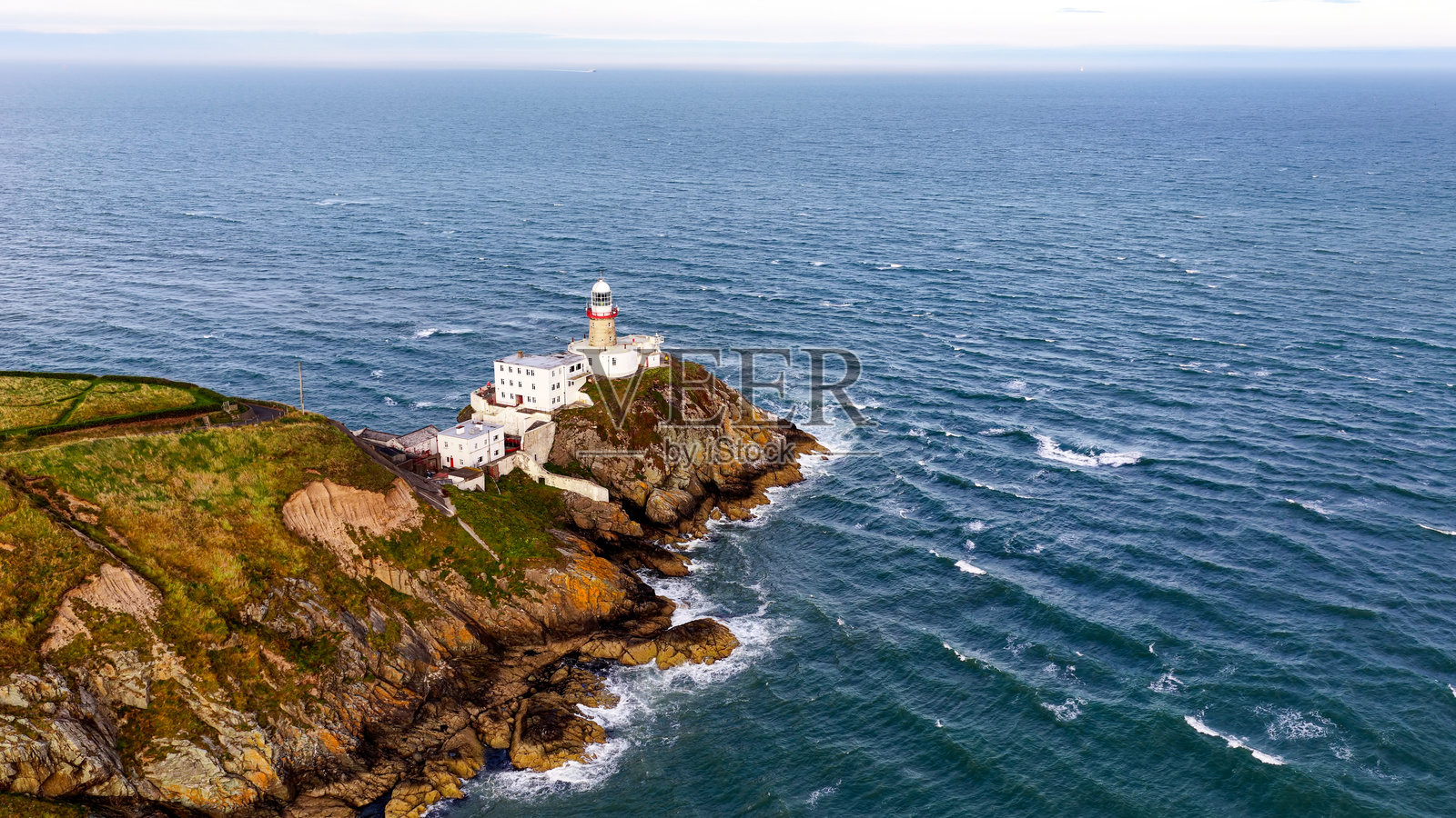 俯瞰爱尔兰都柏林霍斯海角半岛的贝利灯塔，一座具有历史意义的海岸灯塔坐落于壮观的海崖上，享有全景海景，是航海、旅行、海事遗产和旅游业的概念。照片摄影图片