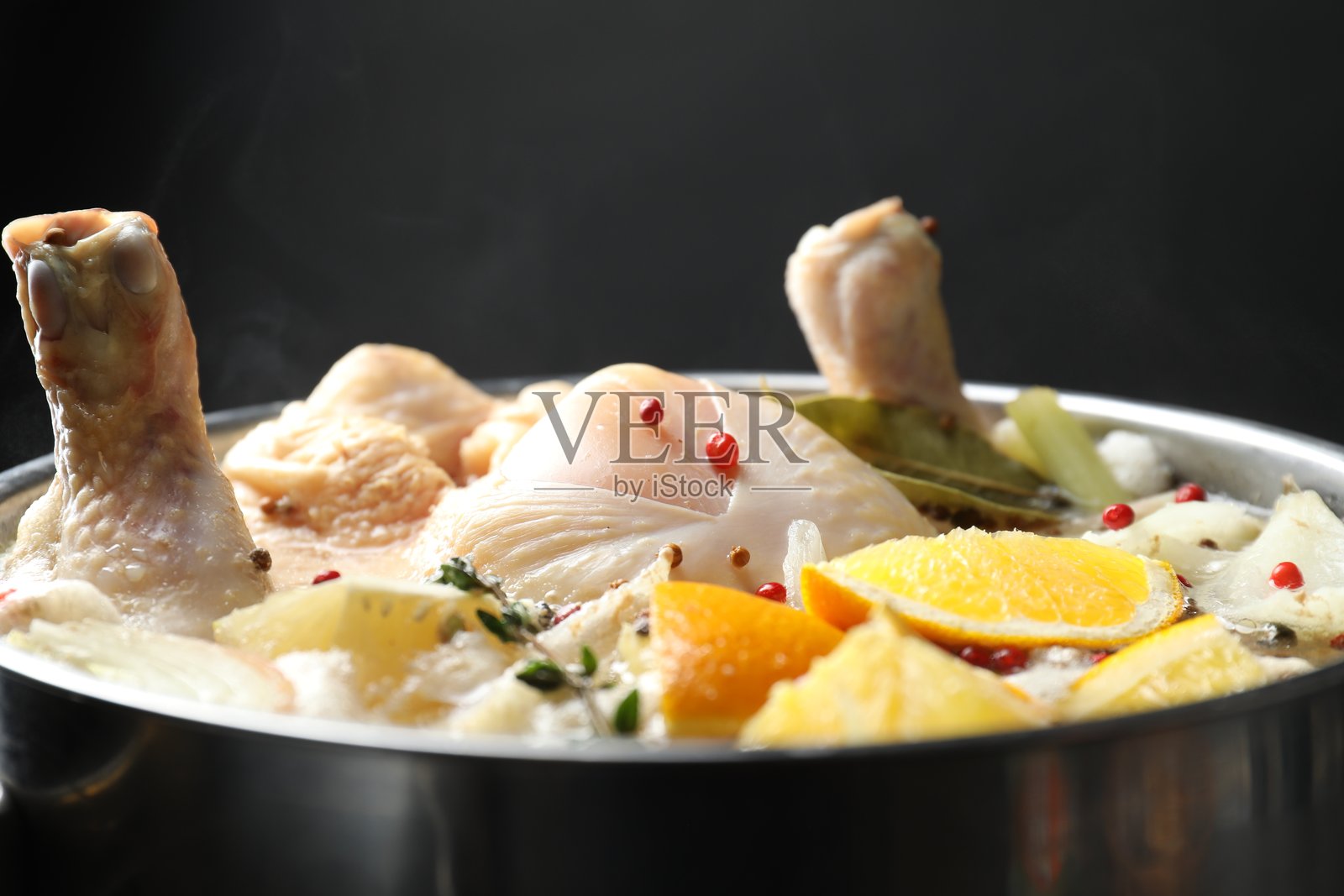 黑色背景下锅中煮沸的整只新鲜火鸡、切好的柑橘类水果和香料，特写照片摄影图片