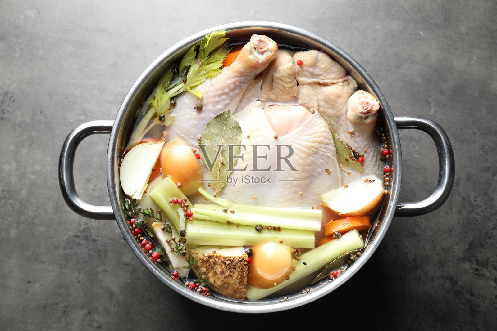 锅里有整只生火鸡、切好的洋葱、芹菜和香料，放在灰色纹理桌上，俯视角度照片摄影图片