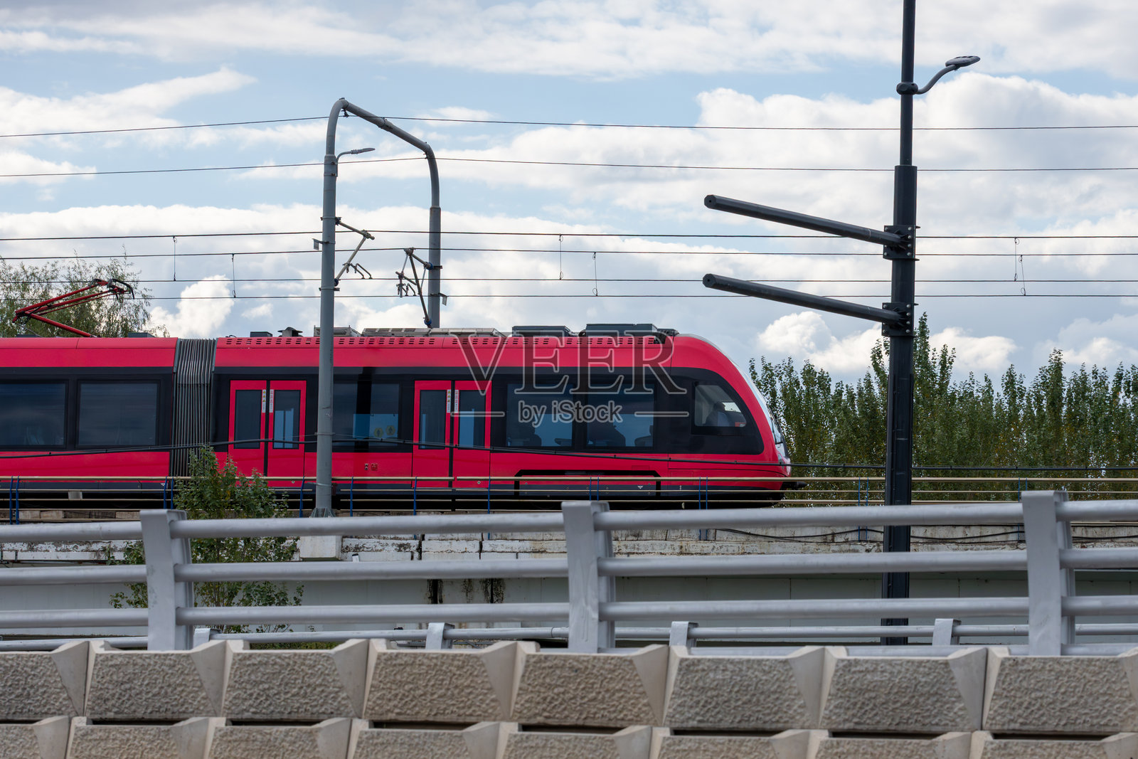 一辆现代化的红色火车在多云的天空下，行驶在架高的轨道上照片摄影图片