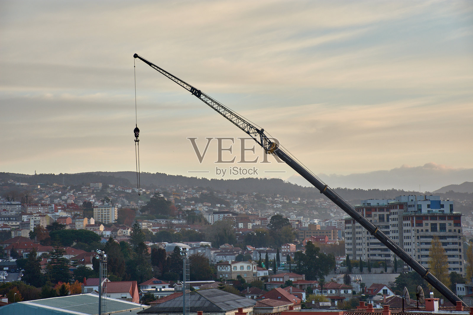 在阴沉潮湿的日子里，金属起重机矗立在住宅区上空，背景是红色的屋顶和山丘。照片摄影图片