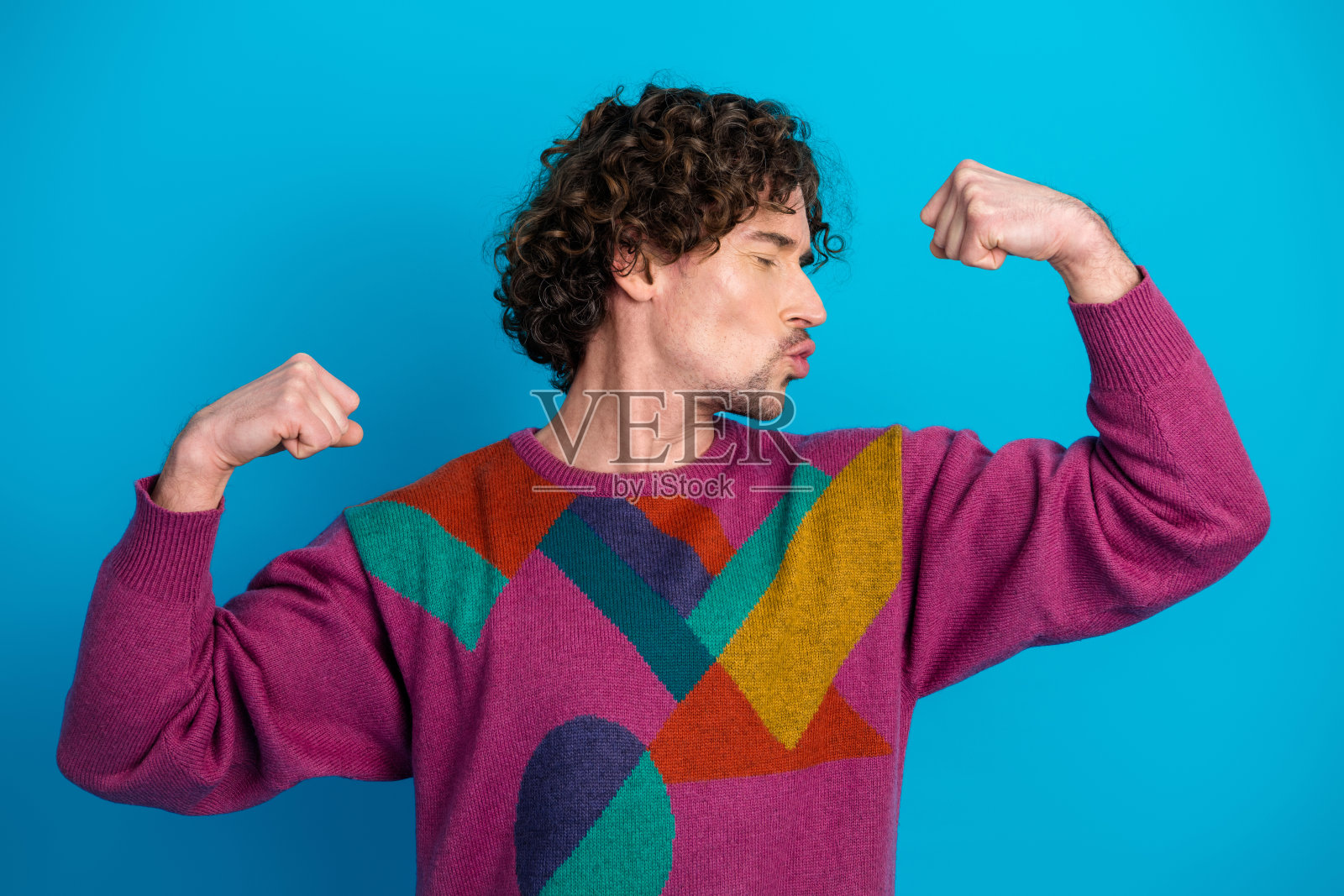 年轻帅气的男子穿着色彩鲜艳的毛衣，在明亮的蓝色背景前展示肌肉照片摄影图片