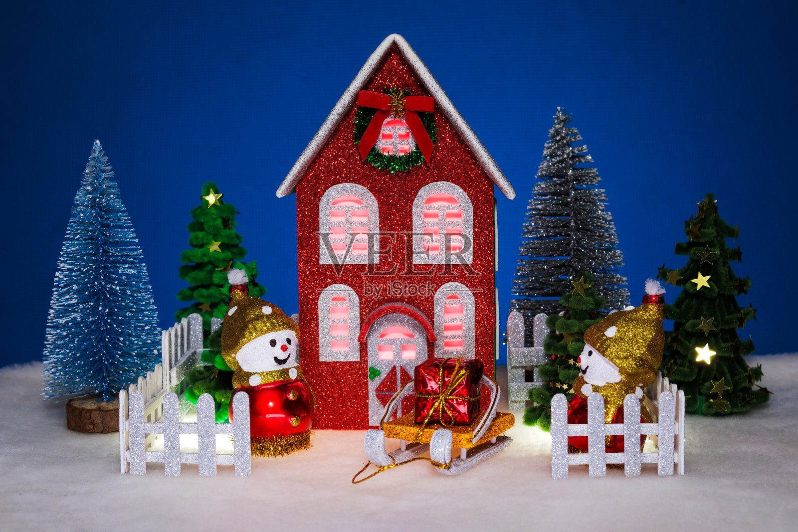 红色的圣诞小屋，有圣诞树和雪人，雪橇上放着礼物，周围有栅栏。照片摄影图片