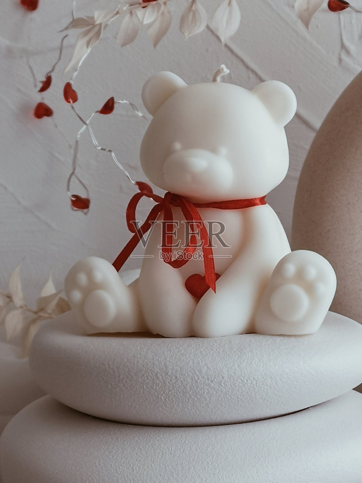 枕头上摆放着一个带有红色丝带的泰迪熊形状的白色蜡烛照片摄影图片