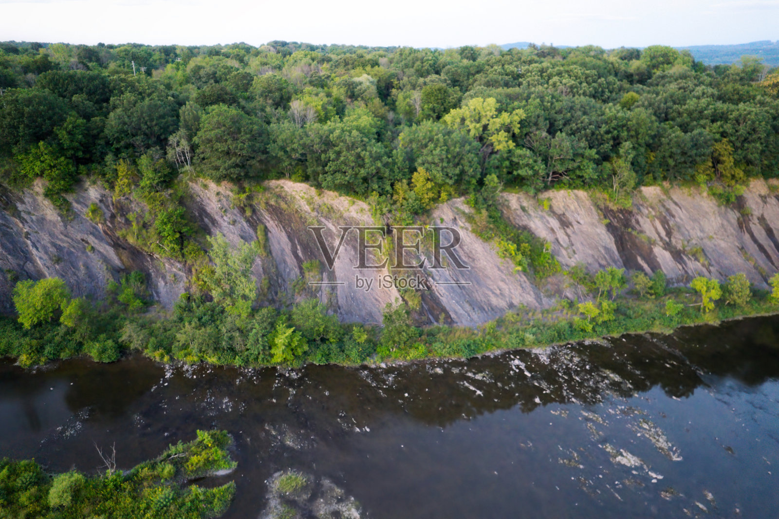 夏日里，无人机航拍视角下，宁静的河流上方悬崖上的隐居之地照片摄影图片
