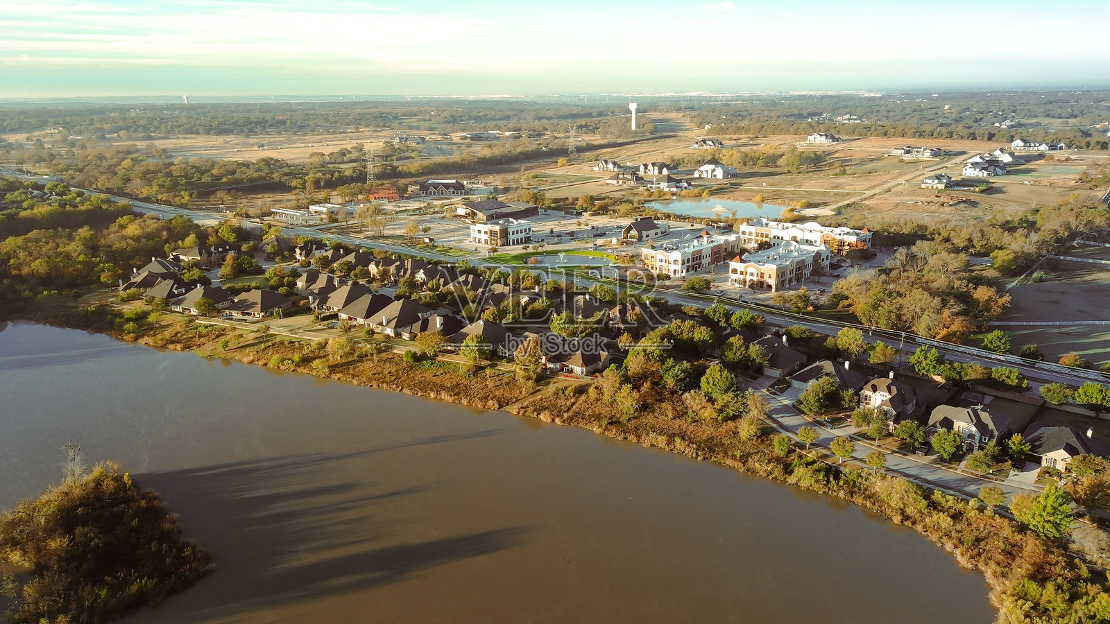 郊区湖畔高档住宅区逐渐过渡到商业区，弯曲的道路、水景和树木缓冲带展示了不断变化的土地利用和社区扩张，德克萨斯州兰塔纳照片摄影图片