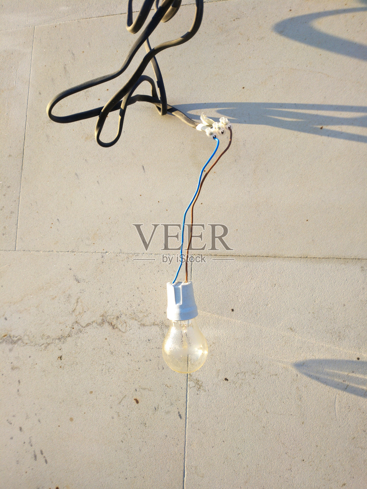 灯泡悬挂在浅色混凝土墙上，沐浴在阳光下照片摄影图片