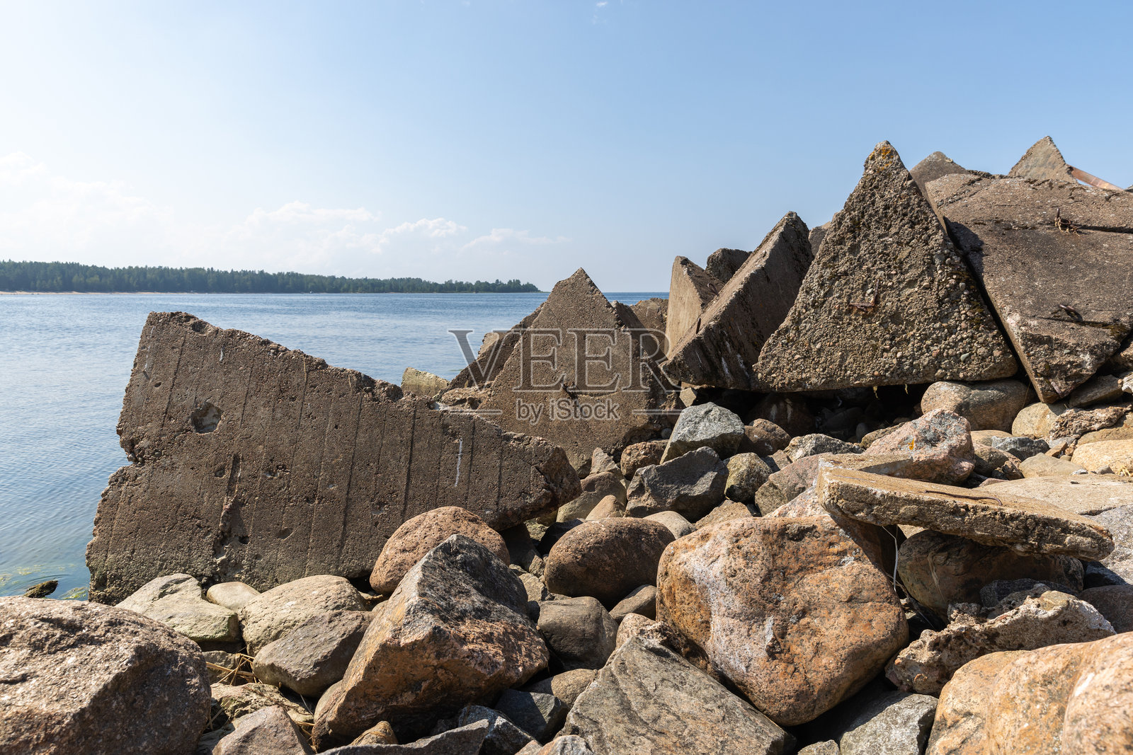平静的蓝色大海边，岩石海岸线上矗立着混凝土防波堤和固石照片摄影图片