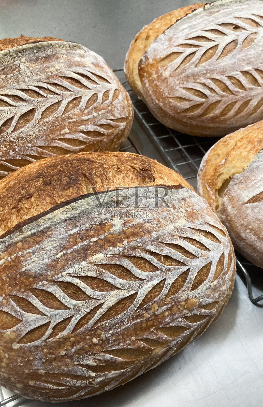 特写镜头展示了手工制作的艺术酵母面包酥脆的外皮，上面有漂亮的割痕图案，烘烤后放在晾网上。照片摄影图片