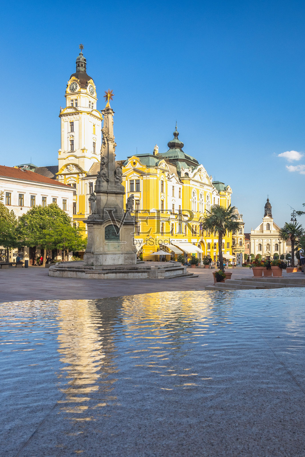 塞切尼广场。城市广场,有历史建筑、中央柱状纪念碑和明亮蓝天下的水景。照片摄影图片