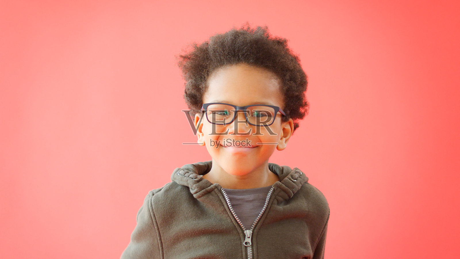 戴眼镜的年轻男孩对着红色工作室背景微笑肖像照片摄影图片