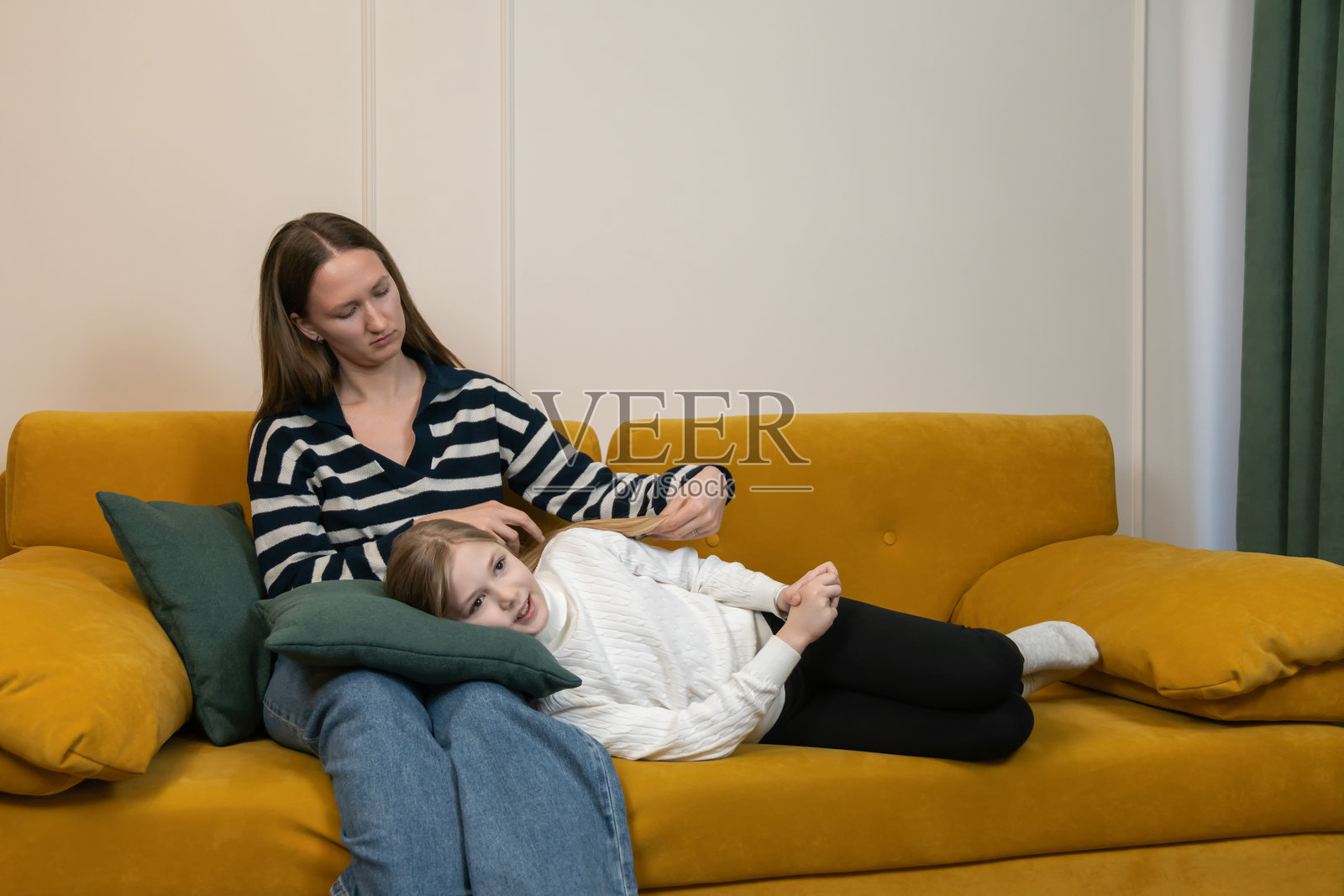 妈妈在温馨舒适的客厅里，温柔地抚摸着女儿的头发，两人依偎在舒适的黄色沙发上，共享着温馨的亲子时光。照片摄影图片