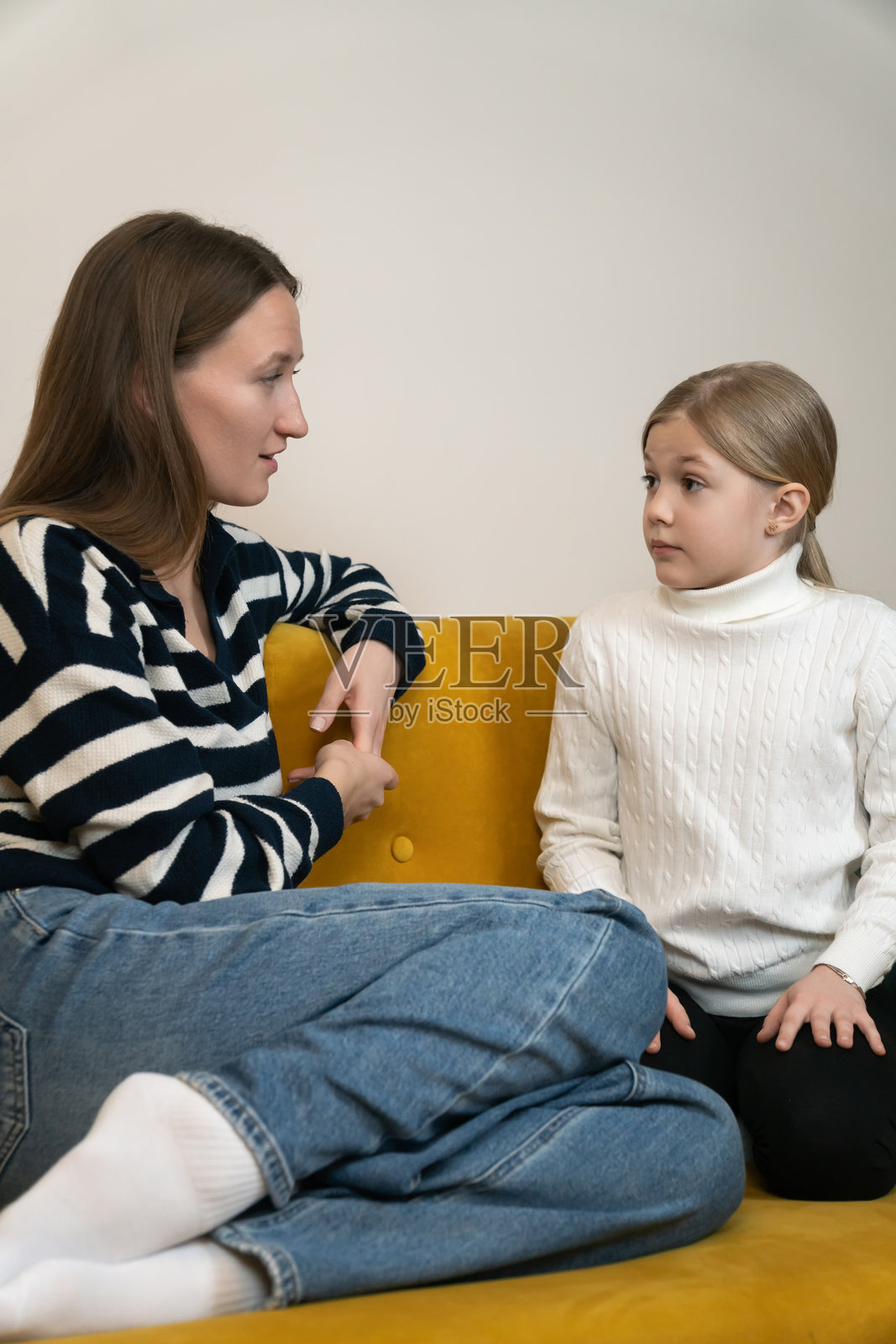 母亲和女儿在家中面对面坐在黄色沙发上，进行着一次衷心的谈话，倾听并给予支持，这是一个坦诚而感人的家庭时刻。竖构图照片照片摄影图片
