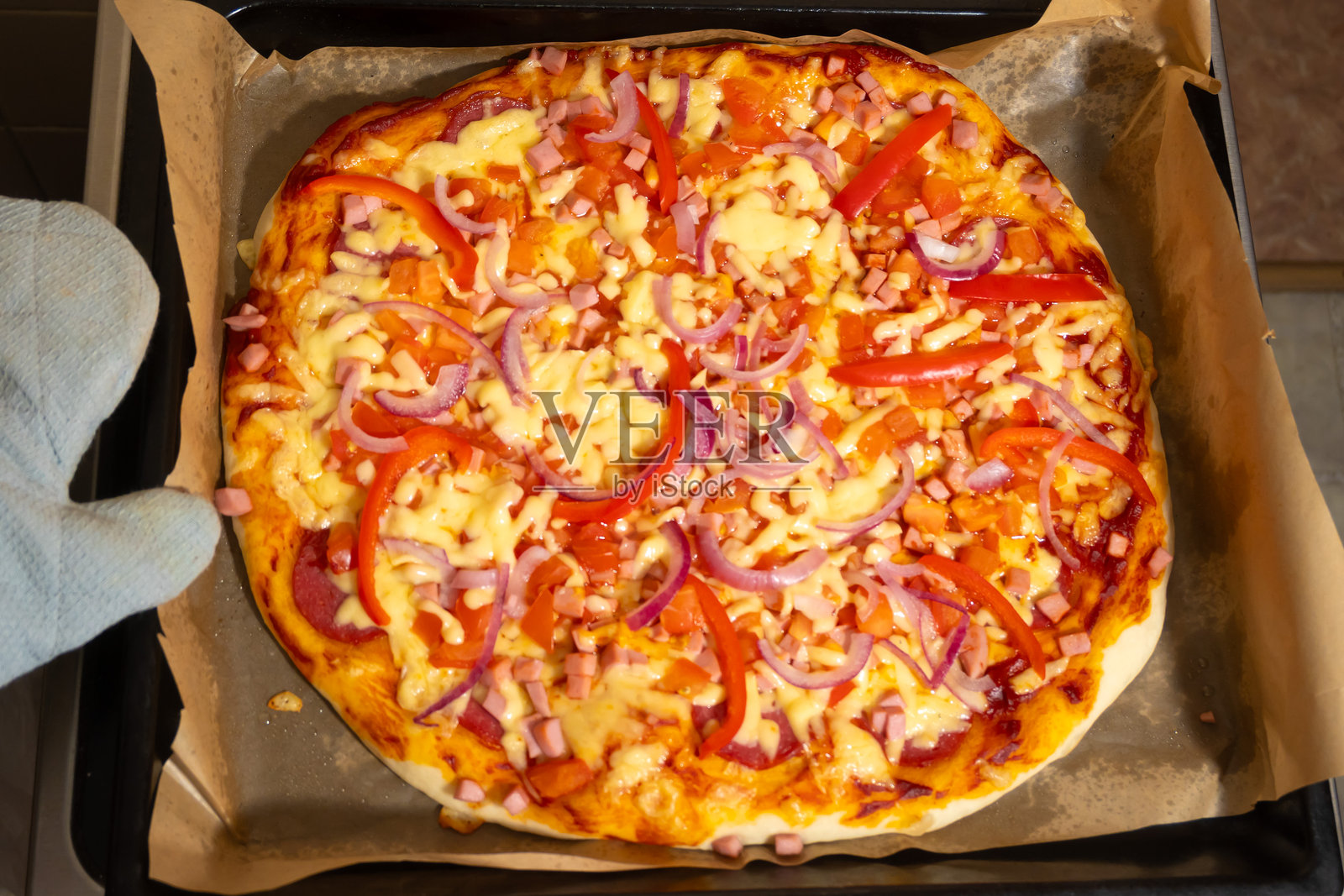 刚出炉的披萨，上面有奶酪和蔬菜，戴着隔热手套照片摄影图片